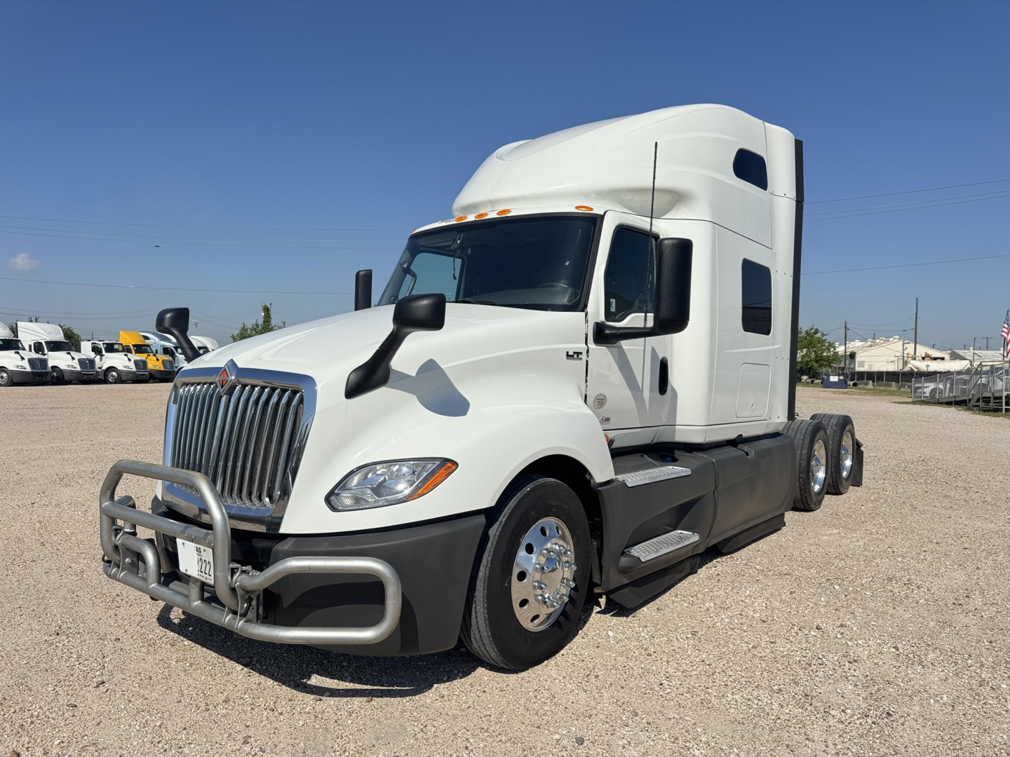 International LT series truck in white with aerodynamic sleeper cab, front grille guard, large side mirrors, and dual rear axles on gravel lot.
