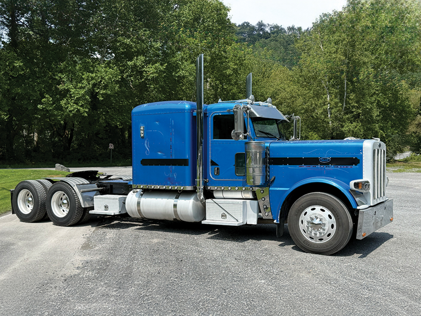 Blue 2010 Peterbilt 389 Extended Hood truck, side view with sleeper cab, chrome exhaust stacks, aluminum fuel tanks, and dual rear axles.