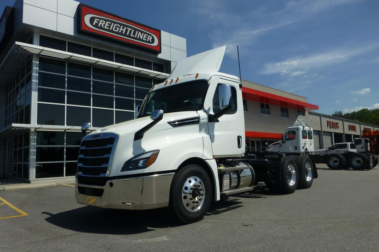 Freightliner Cascadia 126 day cab truck in front of dealership with white paint and aerodynamic hood.