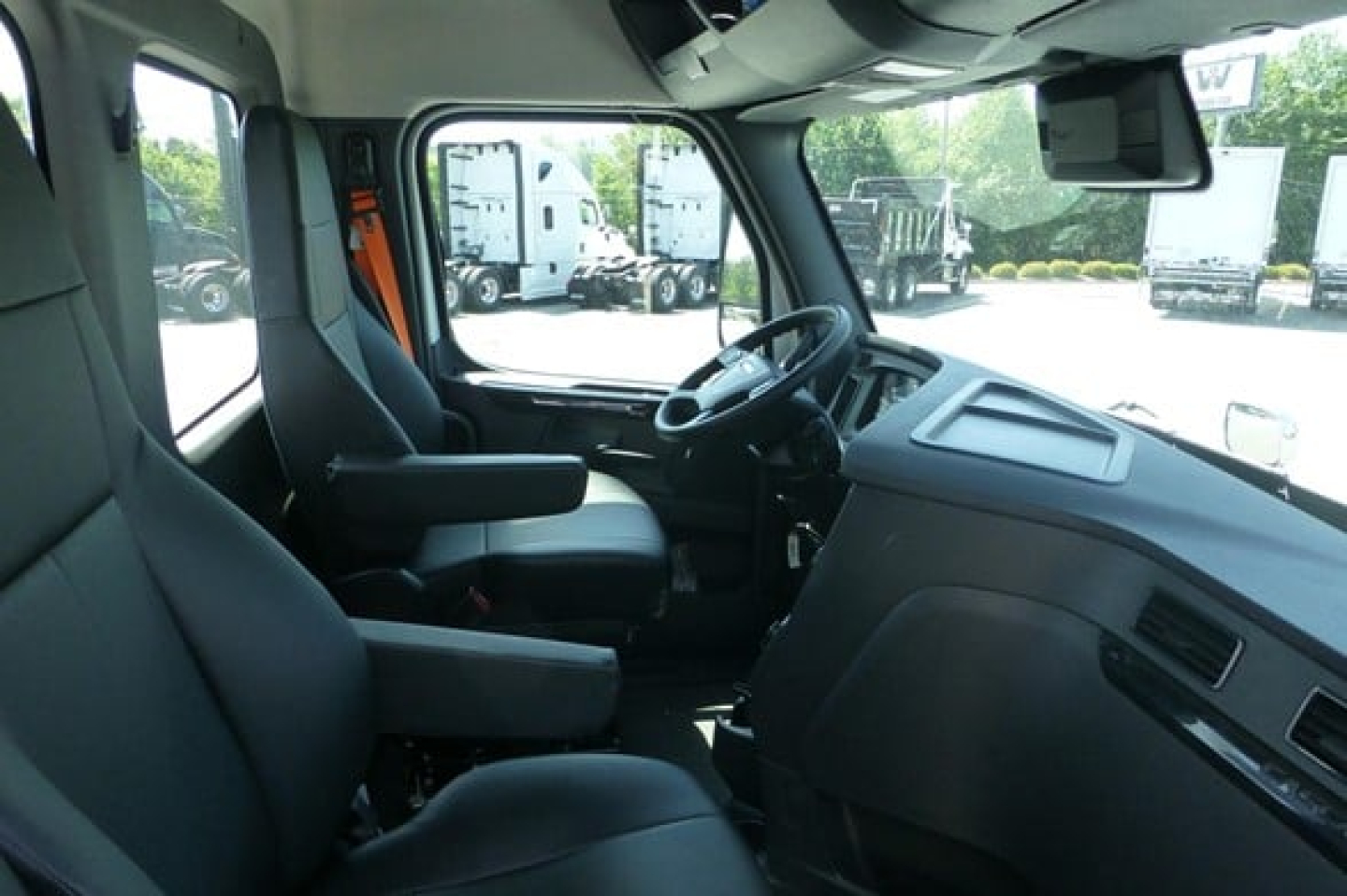 Truck cabin interior showing driver seat, passenger seat, steering wheel, dashboard, and overhead display panel.