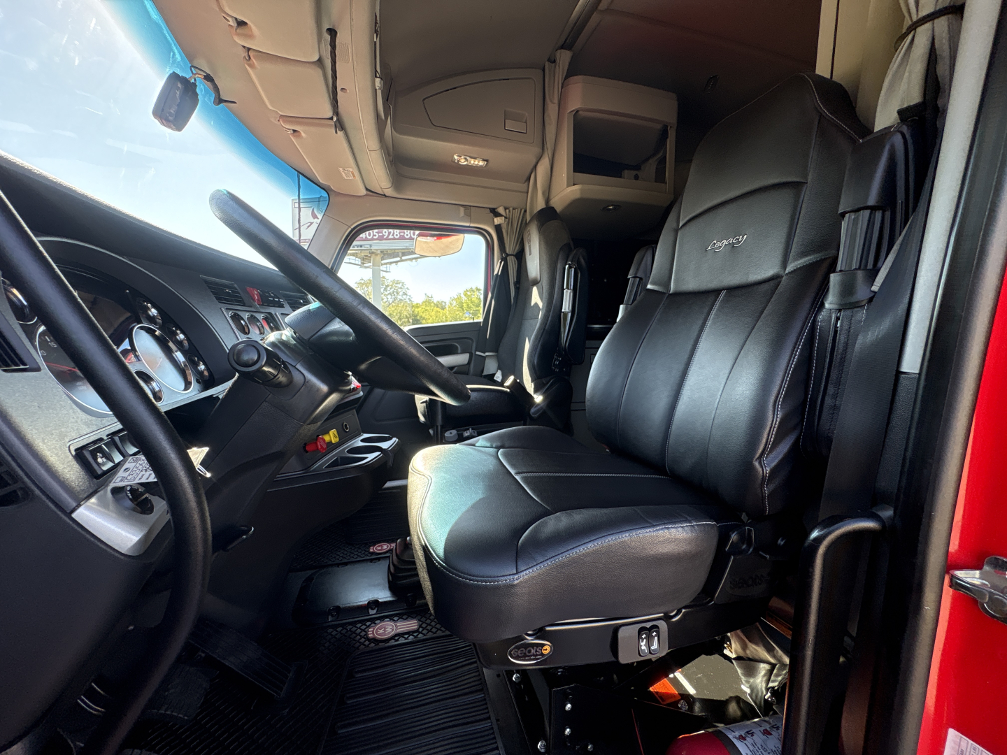Cab interior of a 2022 Kenworth T680 showing driver seat with black leather upholstery, steering wheel, dashboard, and entry area.