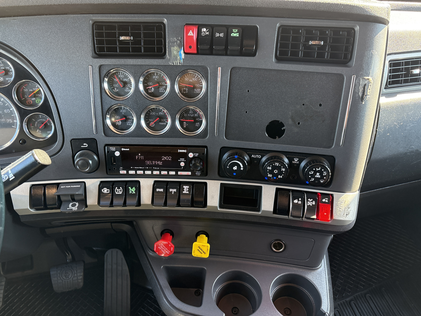 Kenworth T680 dash panel showing multiple gauges, switches, red and yellow drop knobs, and blank radio slot; center console with climate controls and cup holders.