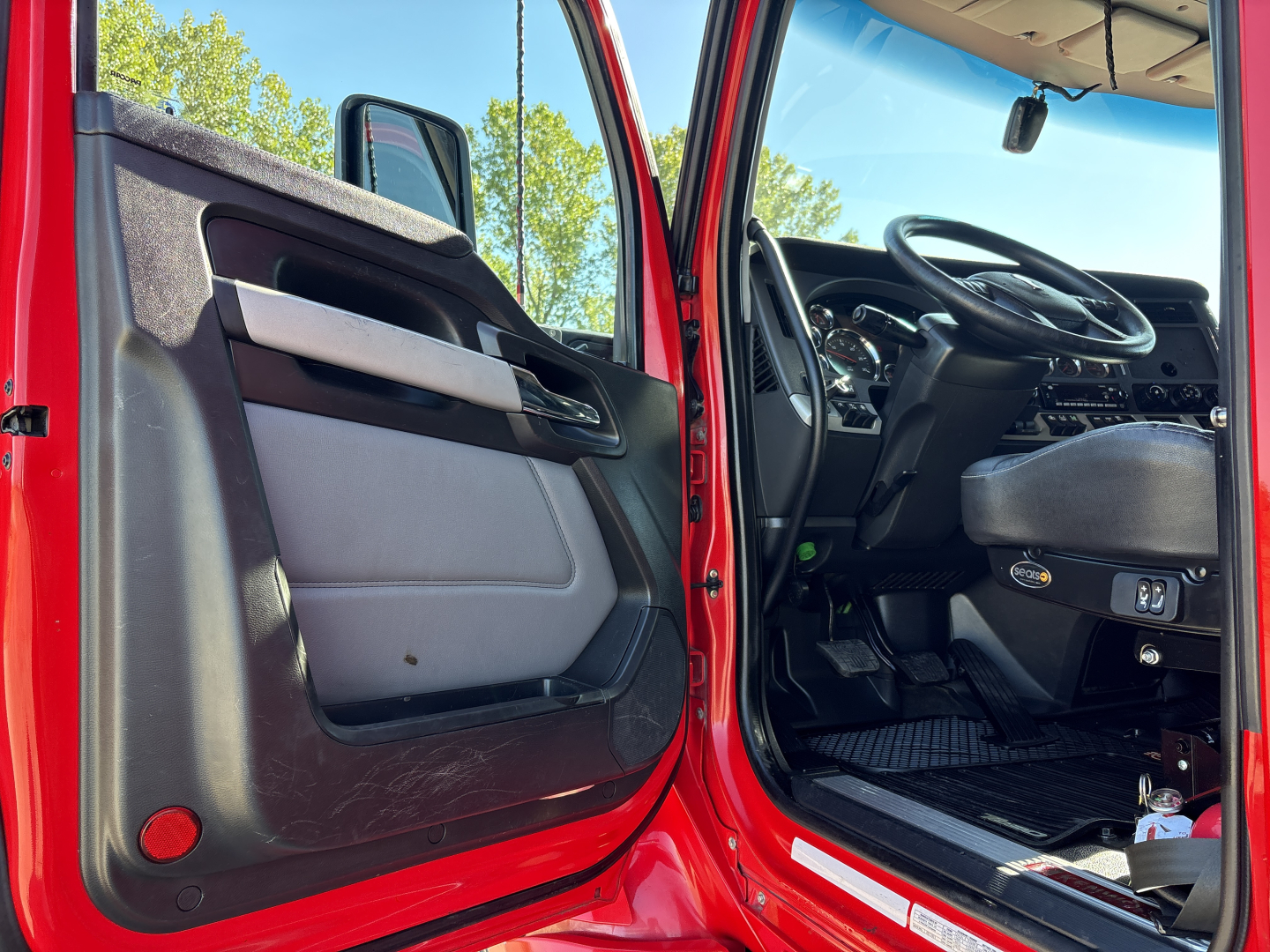 Kenworth T680 truck cab interior visible through open driver door, showing steering wheel, dashboard, and door panel.