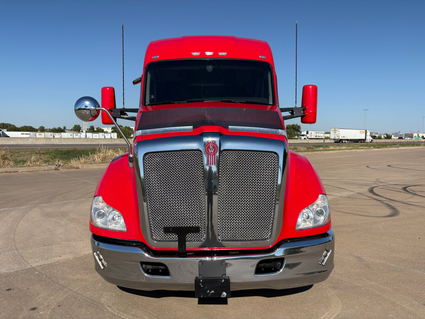 Kenworth T680 front view showing chrome grille and red cab with large side mirrors.