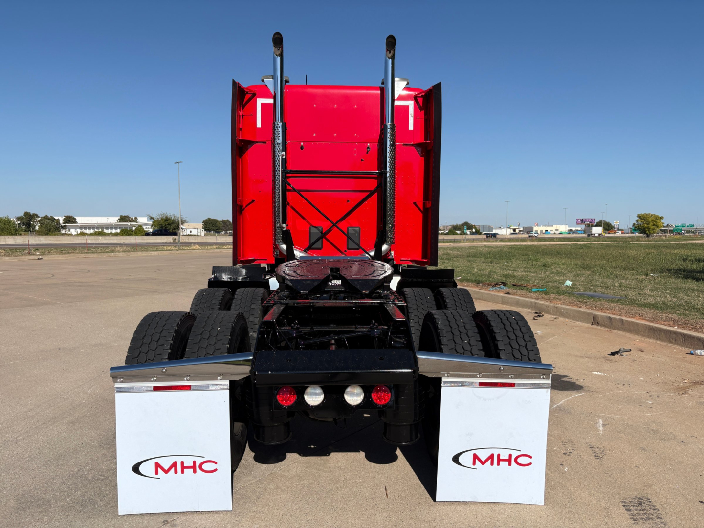Kenworth T680 rear view showing dual rear wheels and red sleeper cab with MHC mud flaps.