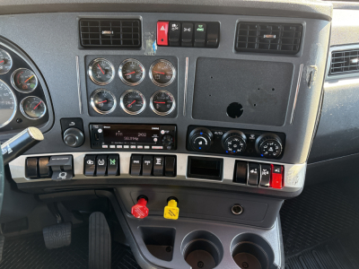Kenworth T680 dash panel showing multiple gauges, switches, red and yellow drop knobs, and blank radio slot; center console with climate controls and cup holders.
