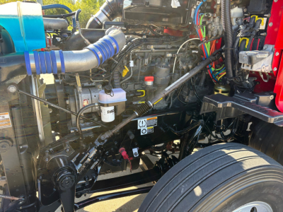 Kenworth T680 engine bay showing intake tube, coolant reservoir, hoses, wiring, and front suspension with wheel.