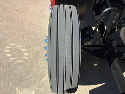 Kenworth T680 front dual axle wheel area showing a single tire with four visible lug nuts and suspension components.