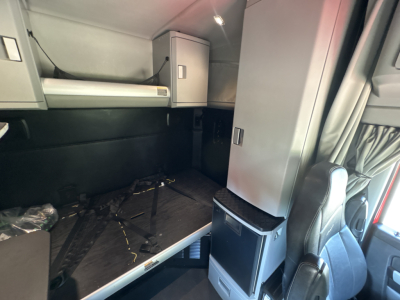Kenworth T680 sleeper cab interior showing bed area, storage cabinets, and compact fridge/coalition unit in cabin.