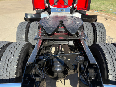 Kenworth T680 rear chassis and drive axles showing dual rear axles, suspension, and fifth wheel with red cab in background.