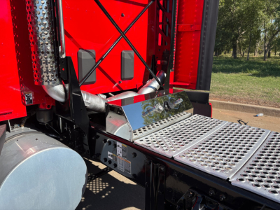 Kenworth T680 sleeper cab showing polished steel step and exhaust stack area with perforated metal steps and red body panel.