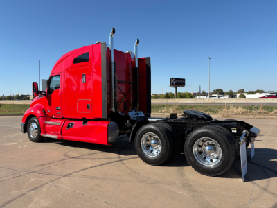 Kenworth T680 tractor in red color, side view, with sleeper cab and dual rear axles, empty fifth wheel, clear sky.