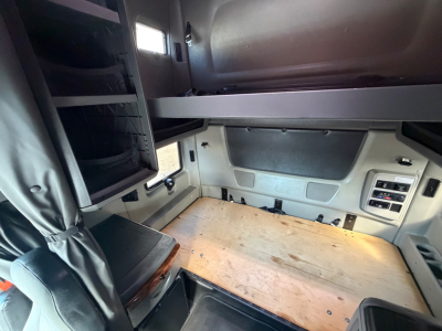Truck cab interior showing a wooden sleeper floor with storage cabinet on left and overhead bunk area in a 2021 International LT625.
