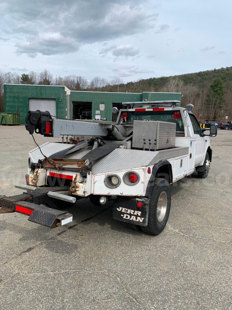 Tow truck rear view showing flatbed with metal ramps and equipment mounted on bed, white cab, black mud flaps, and dual rear wheels.