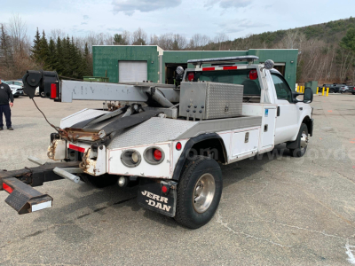 Ford F-350 tow truck with flatbed and hydraulic reel, rear chrome bumper, dual rear wheels, toolbox on bed, VIN plate not visible.