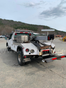 Tow truck rear view showing flatbed with equipment and towing apparatus on white Ford F-350.