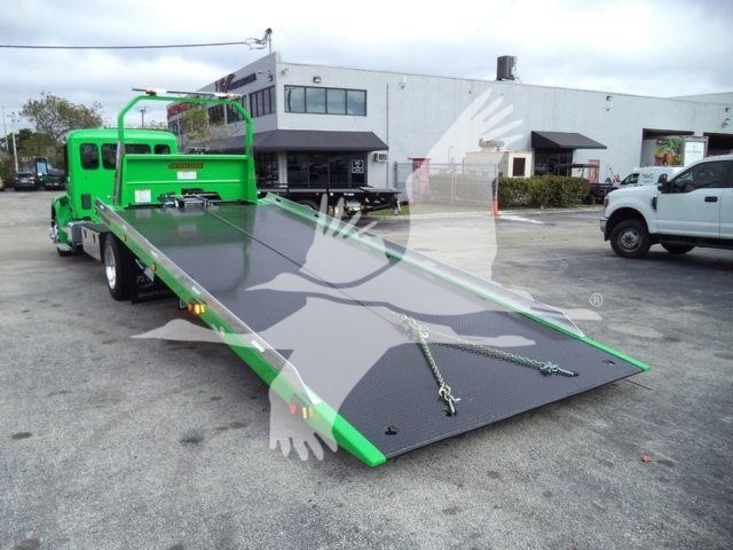 Green rollback tow truck with a lowered flatbed in a parking lot showing brand-new Peterbilt 536 equipment, rollout ramp and loading deck.