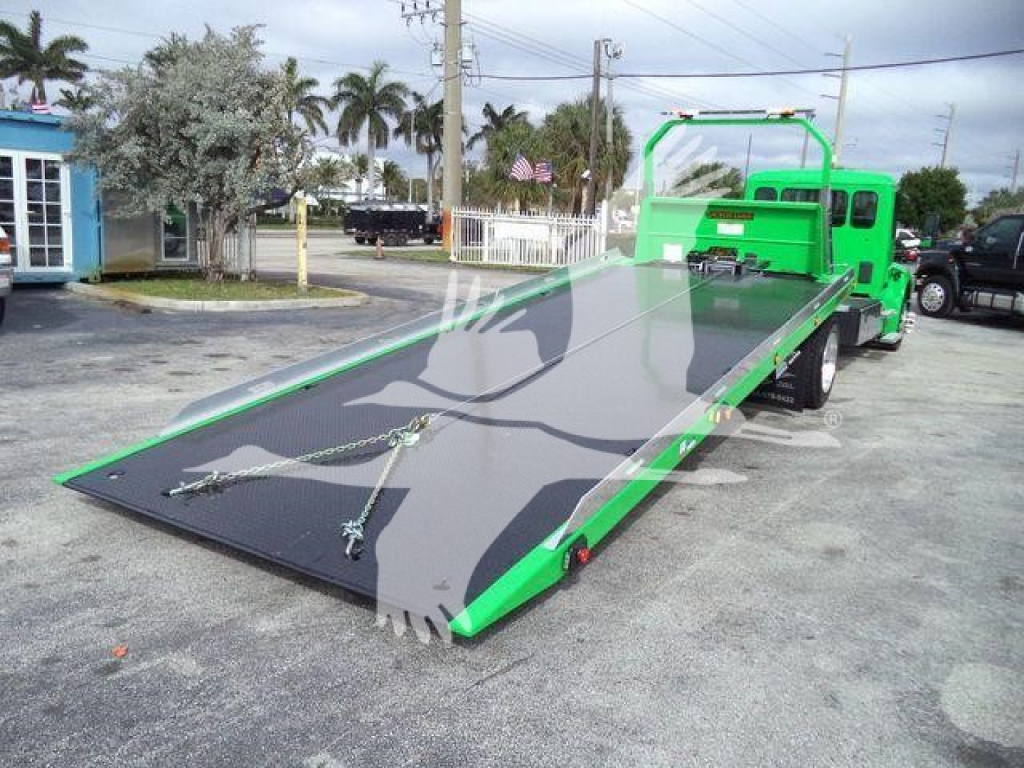 Tow truck with a loading ramp, green cab and bed, flatbed rollback tow unit, stock image showing large folded metallic ramp and towing equipment on a paved lot.