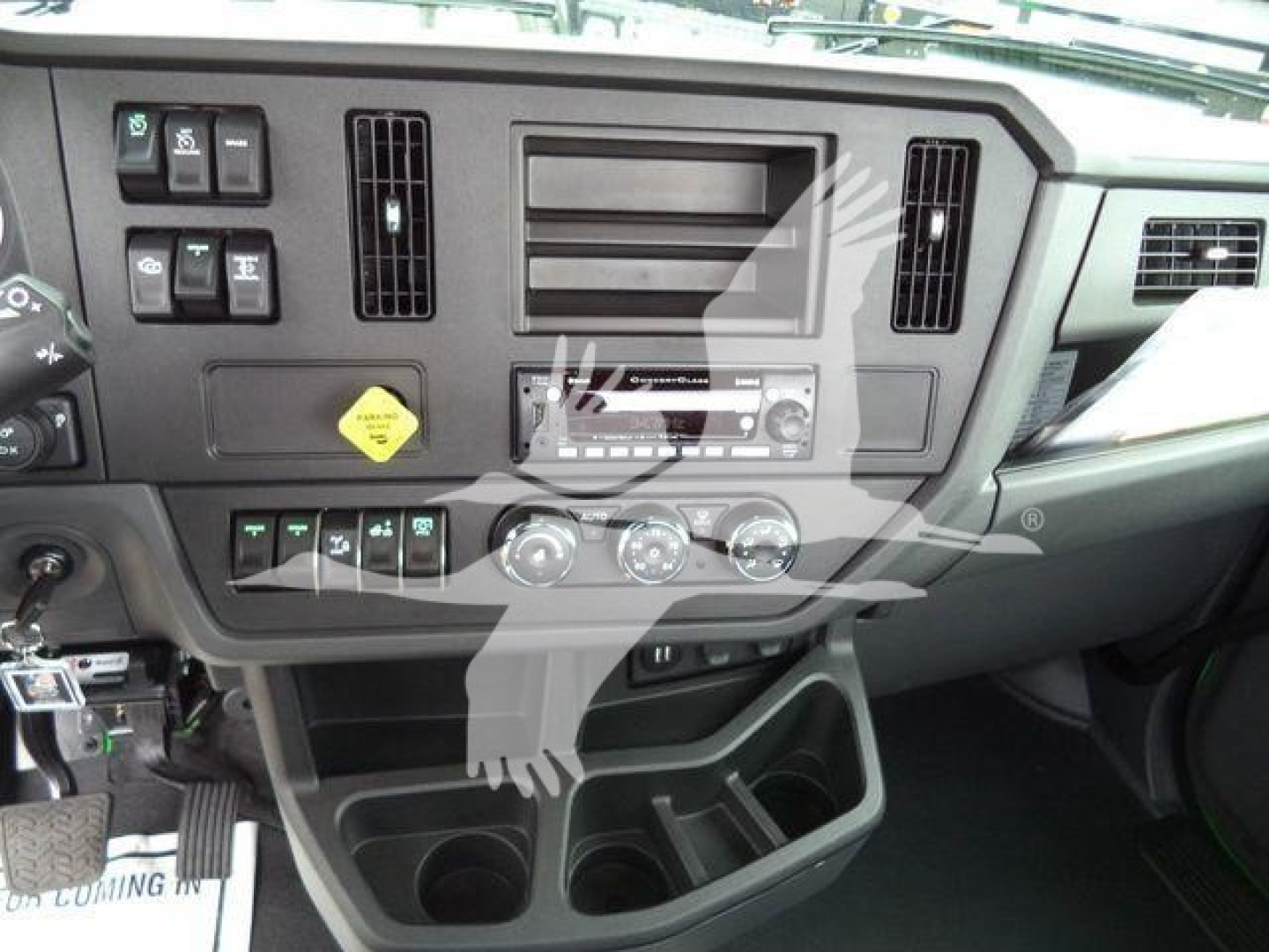 Dashboard of a Peterbilt truck cab with center console, radio, climate controls, and various switches; visible text includes warning label, knobs, and blank stereo slot
