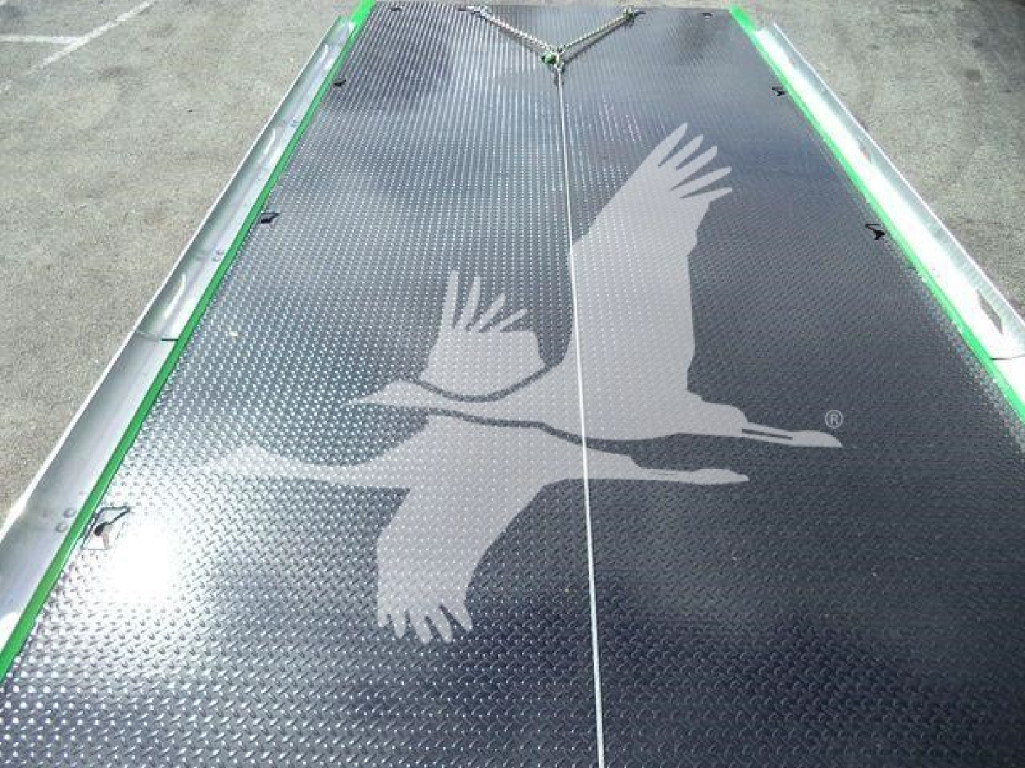Flatbed or deck surface with diamond plate pattern and a large white bird silhouette graphic, green edge trim along sides.