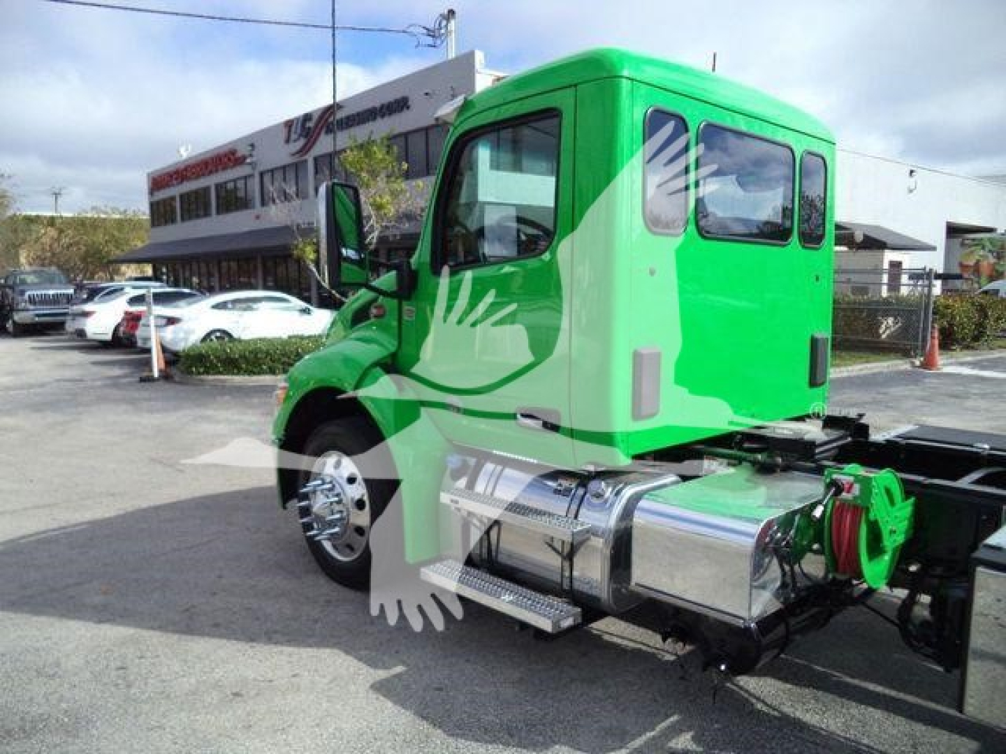 Green Peterbilt 536 cab in truck lot, side rear exhaust tank, chrome fuel tanks, rollback truck chassis visible.