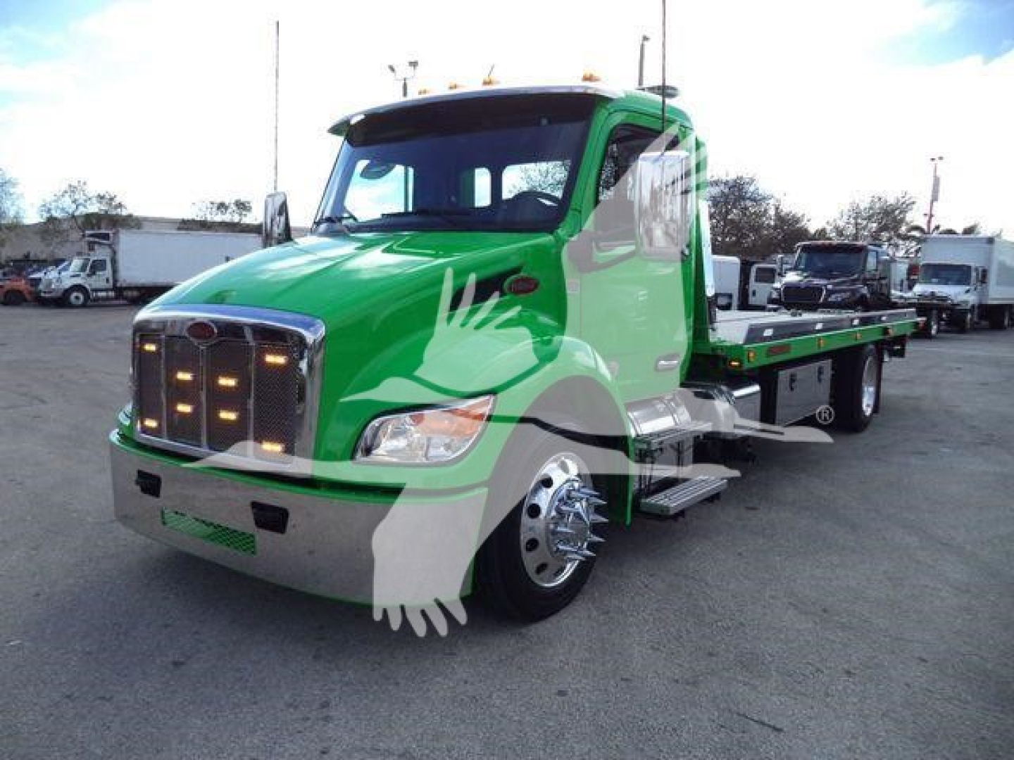 Green Peterbilt 536 rollback truck shown in a parking lot with a long green flatbed and chrome front grille.