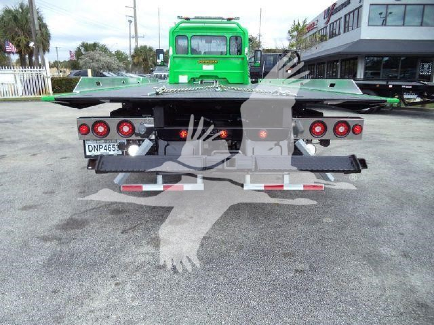Rear view of a green Peterbilt rollback truck with flatbed and dual taillights, license plate DNP465 on a concrete lot.