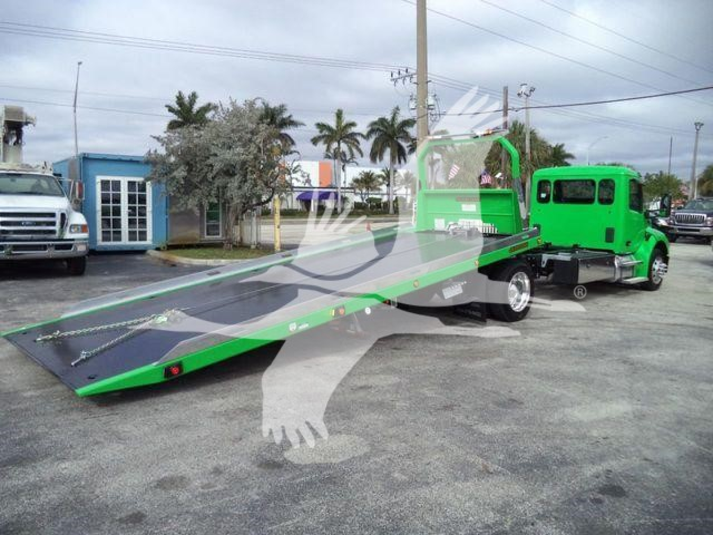 Truck and rollback transport with a bright green tow truck attached to a green flatbed carrier, awaiting operation.