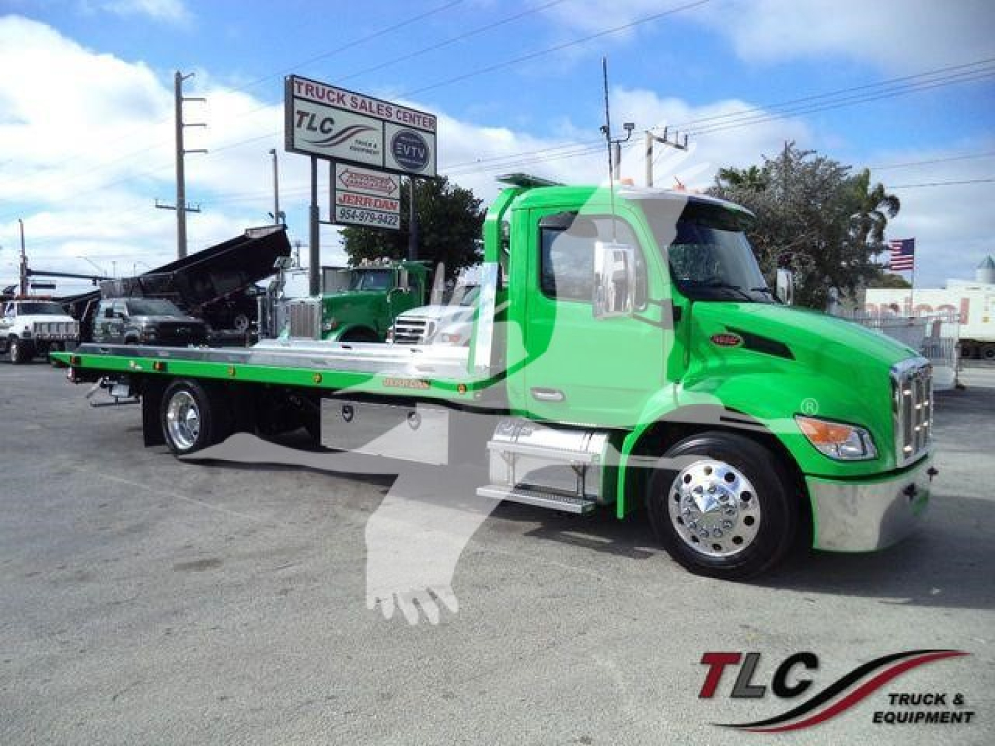 Peterbilt 536 rollback truck in bright green with flatbed at a dealership lot, showing carrier truck sign in background.