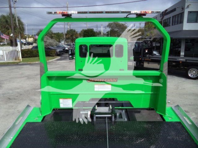 Green Peterbilt rollback truck rear view showing flatbed and overhead rollover guard with branding plate visible.