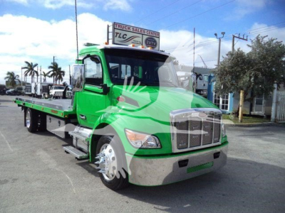 Peterbilt 536 rollback truck in green, front view with extended flatbed and chrome bumper, dealership lot in background.