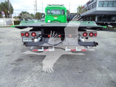 Rear view of a green Peterbilt rollback truck with flatbed and dual taillights, license plate DNP465 on a concrete lot.