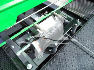 Equipment winch or hoist assembly mounted on a green Peterbilt 536 rollout truck, showing a metal winch drum with cable, bolts, and mounting brackets on a diamond plate surface.