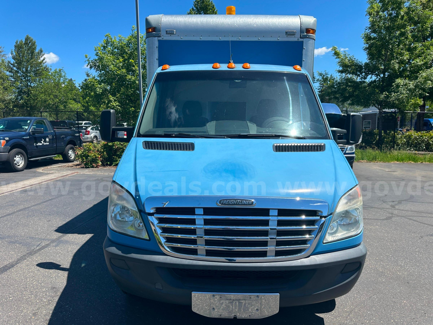 Freightliner Sprinter front view showing blue cargo van with grille, headlights, and windshield; dash badge not visible.