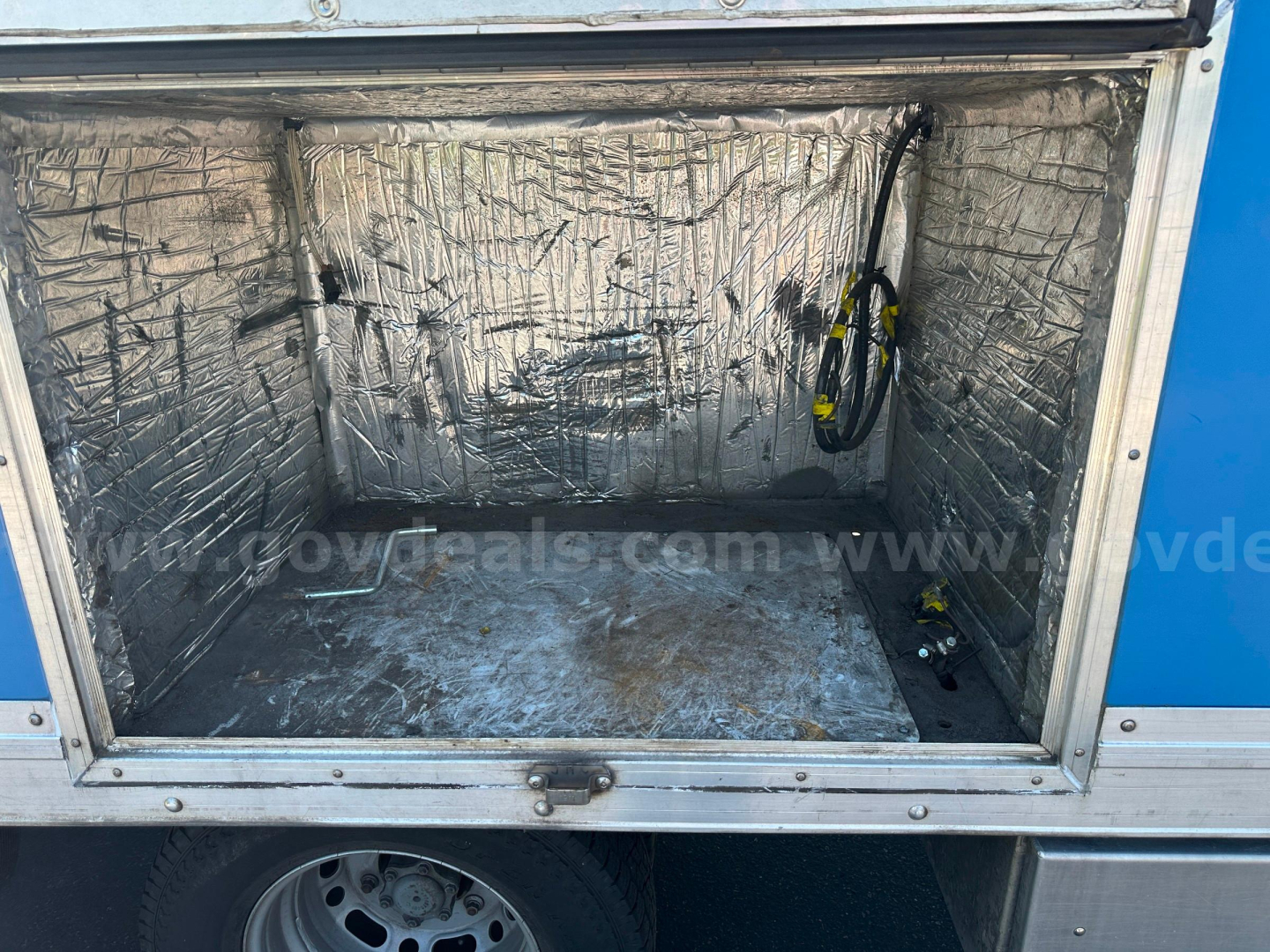 Trunk/storage area of a 2008 Freightliner Sprinter van with reflective insulation lining and a strap hanging on the right side.