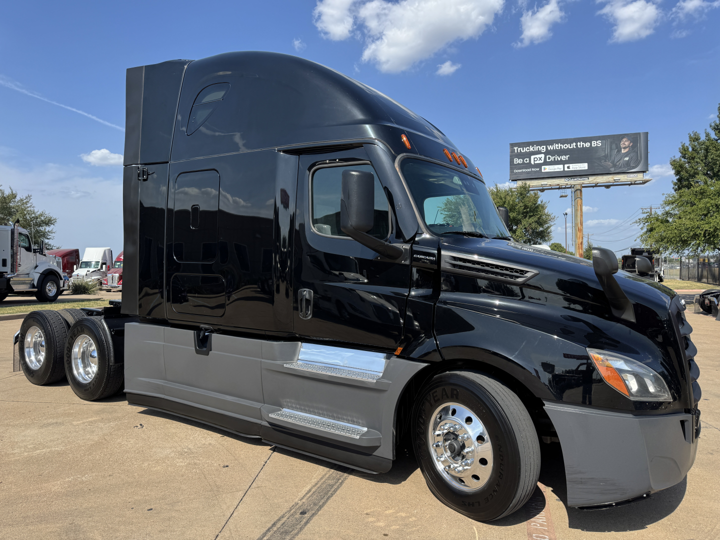 Truck cab side view of a black Freightliner PT126064ST sleeper, glossy finish, with chrome fuel tanks and front wheel, day time outdoor lot.
