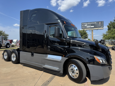 Truck cab side view of a black Freightliner PT126064ST sleeper, glossy finish, with chrome fuel tanks and front wheel, day time outdoor lot.