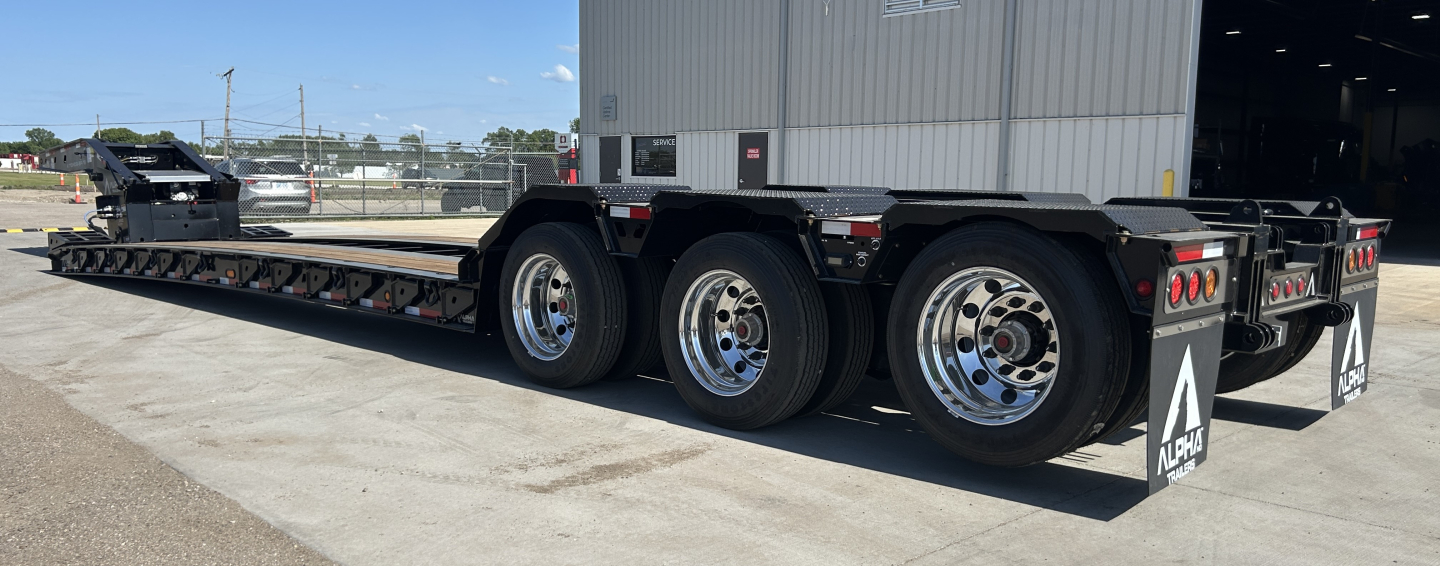 Trailer showing wheels and lowboy bed with Alpha branding; text visible includes 'NO SIGNAL' and reflective placards on mudflaps, various tires, and structural components
