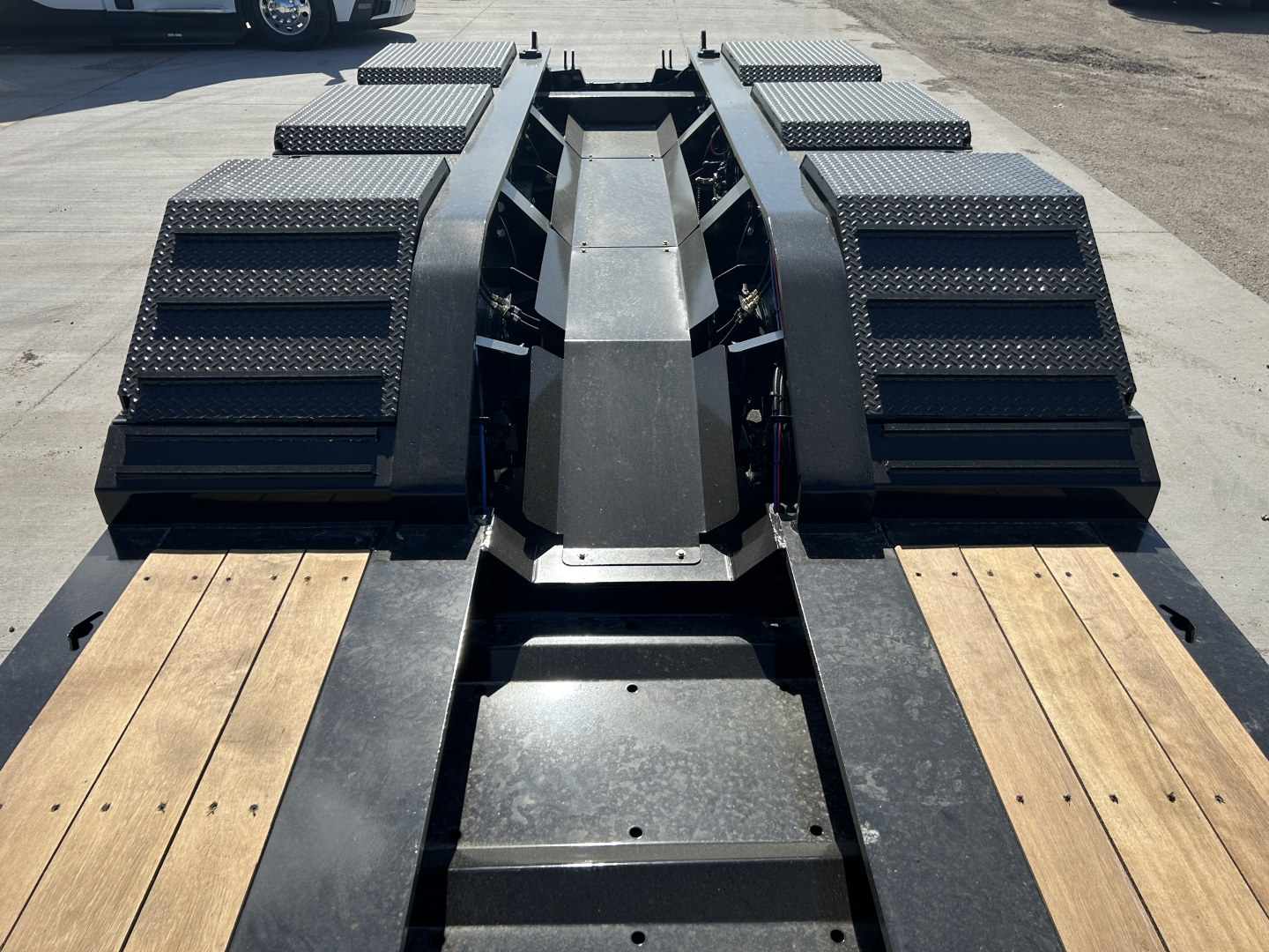 Trailer chassis and fender sections of a lowboy trailer with reinforced black steel and wooden decking, central spine and wheel wells visible.