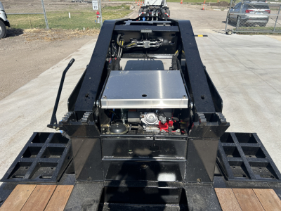Front view of a lowboy trailer hitch area with a metallic toolbox, hydraulic components, and black steel frame; visible control lever and structural beams.