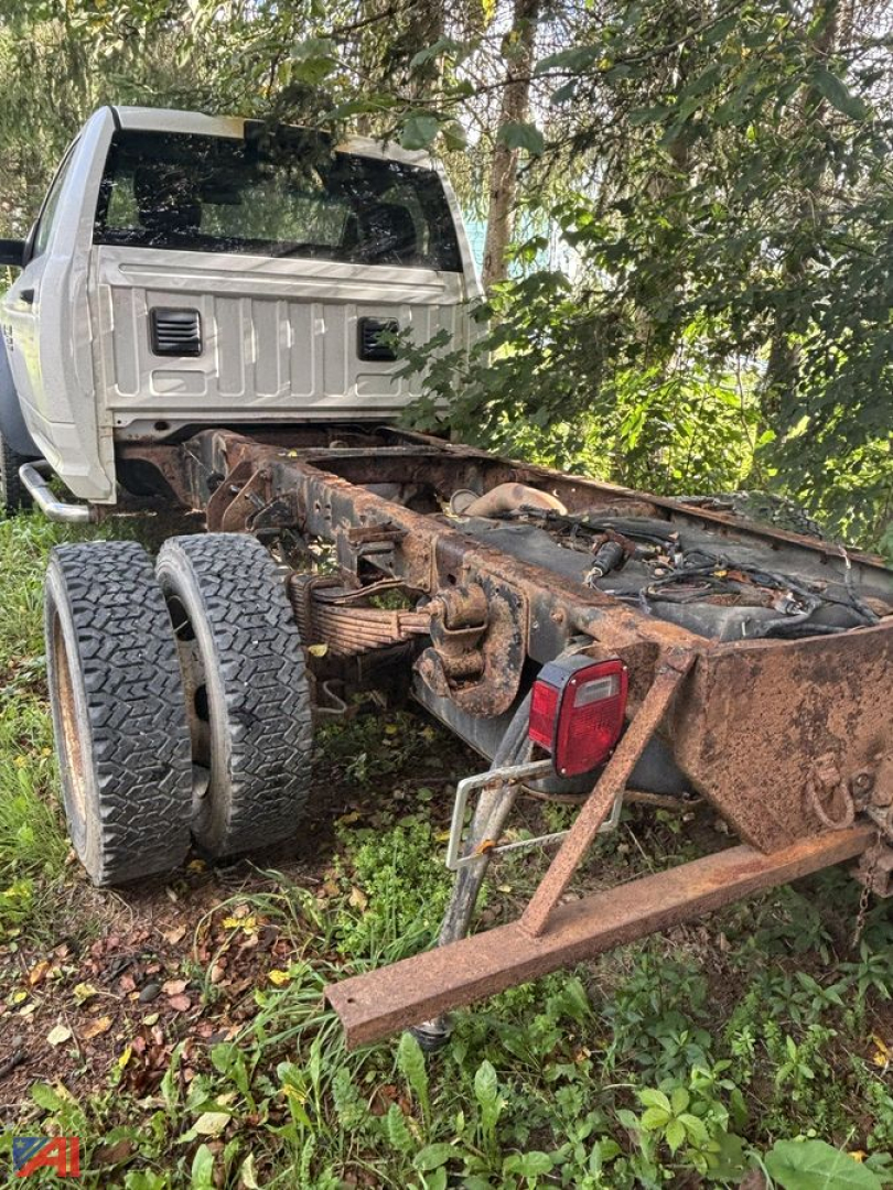 Cab and chassis truck rear view showing exposed frame rails, dual rear wheels, and plow hitch with rusted frame components.
