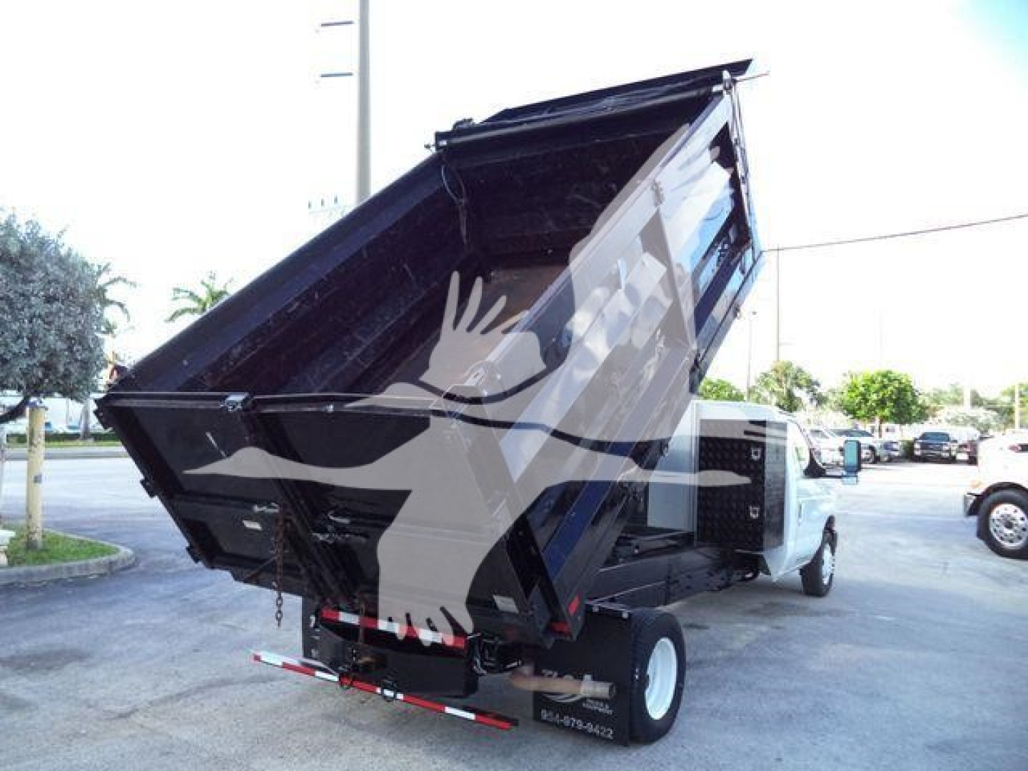 Ford E450 dump truck with raised bed showing cargo area and rear hitch; front cab visible with wheels in a dealership lot.