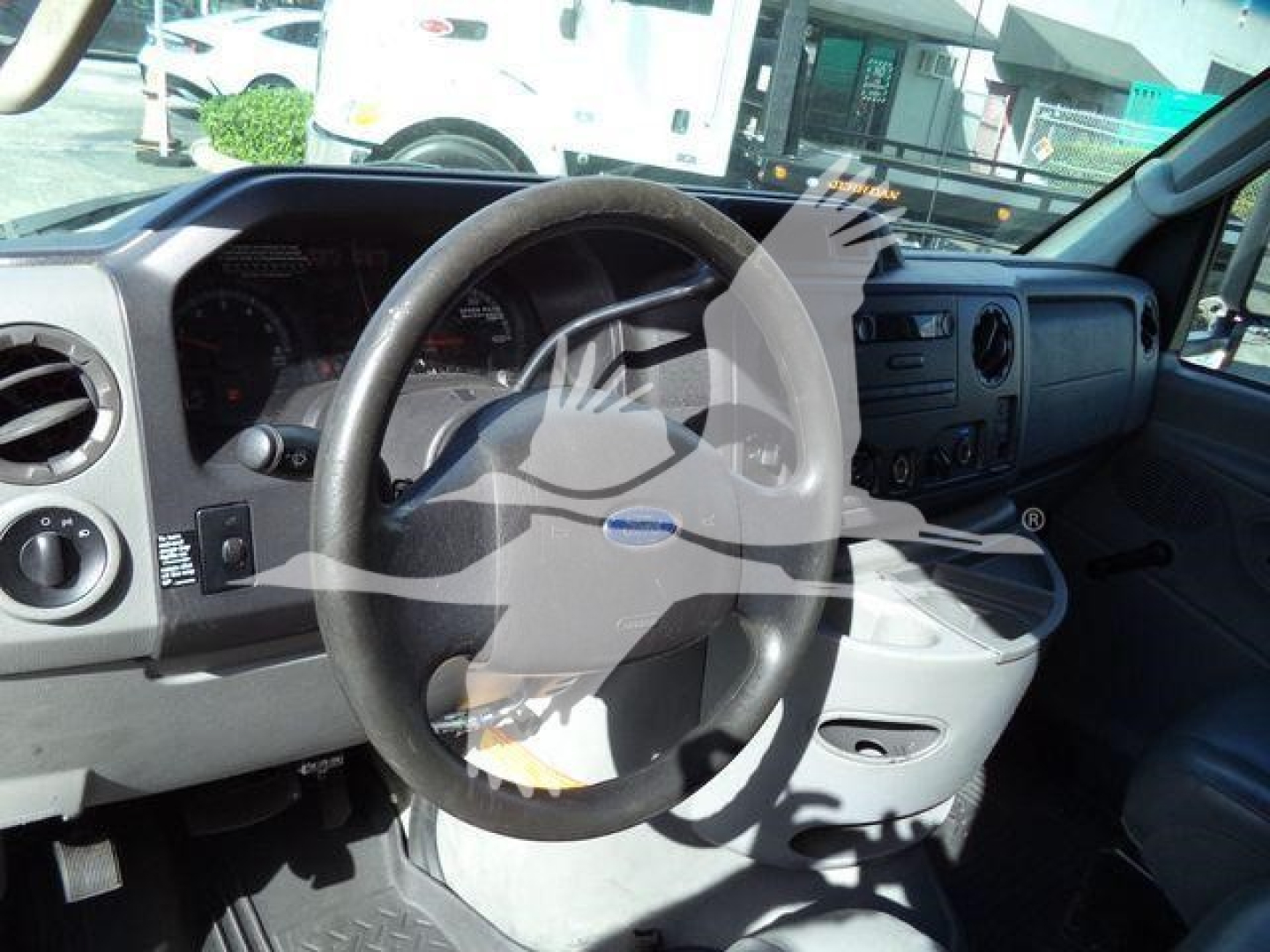 Ford E-Series interior showing steering wheel, dashboard, and center console; dashboard features gauges and vents; factory steering wheel with Ford emblem visible.