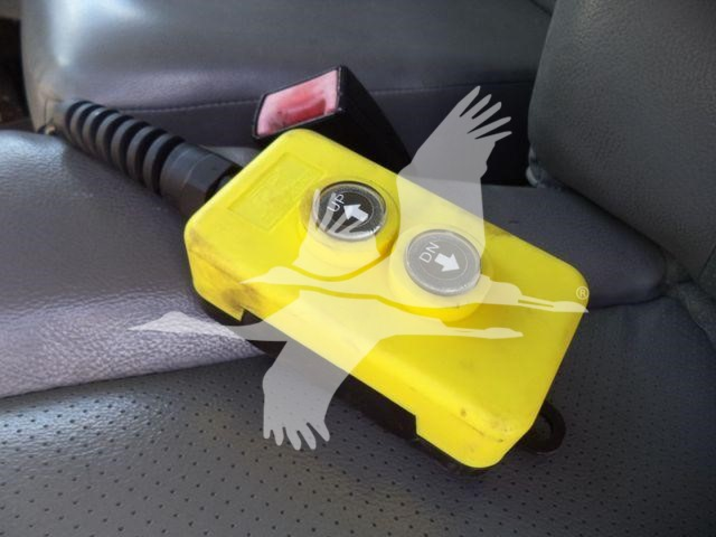 Yellow portable auxiliary fuel or water tank with two circular caps labeled ON and OFF, attached by a cord; mounted in vehicle interior near seat.