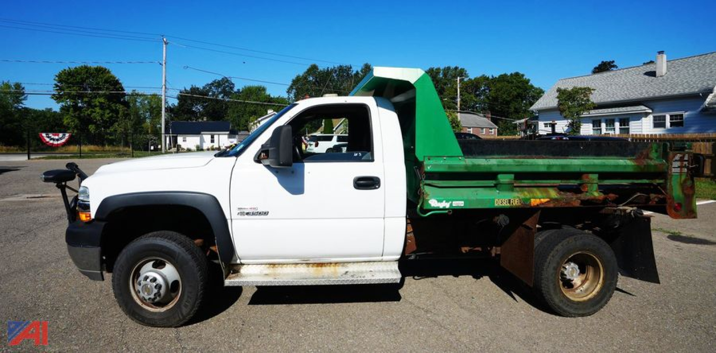 Dump truck: 2002 Chevrolet Silverado 3500 with white cab and green dump bed, side profile view showing rust and dirt on bed and wheel wells.