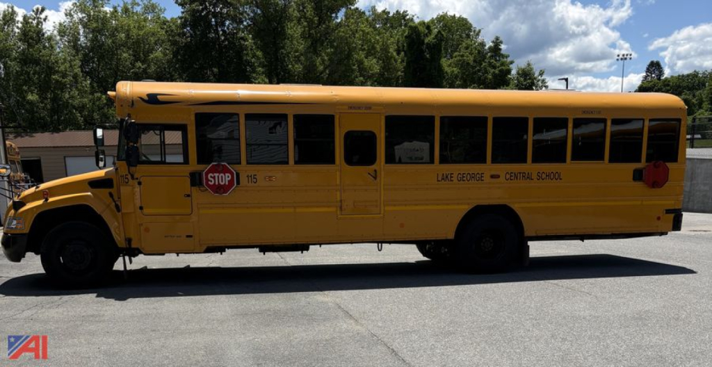 School bus side view showing yellow body with doors and windows, stop sign extended, Lake George Central School logo.