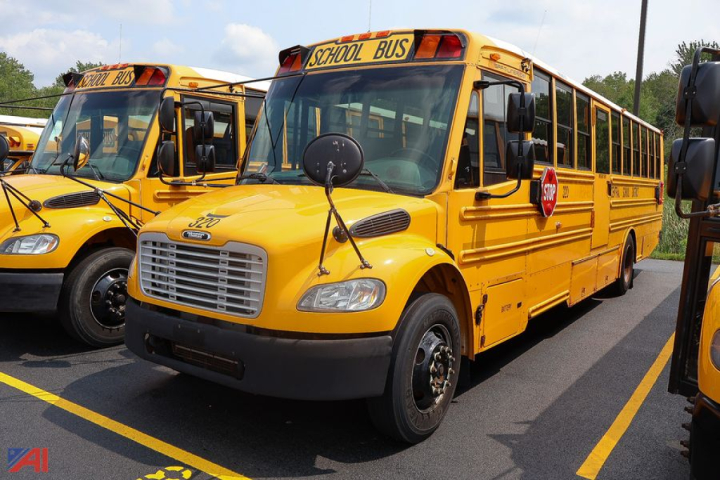Yellow Freightliner Thomas Saf-T-Liner school bus, front left view, with 'SCHOOL BUS' stop sign and black grille; other buses in background.