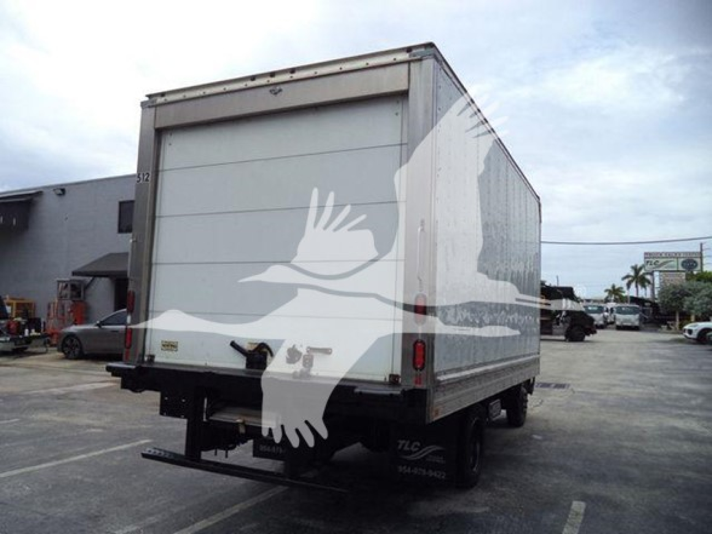 Rear view of a white refrigerated box truck with a roll-up door, black bumper, and dual rear wheels. No visible branding text legible on the image.