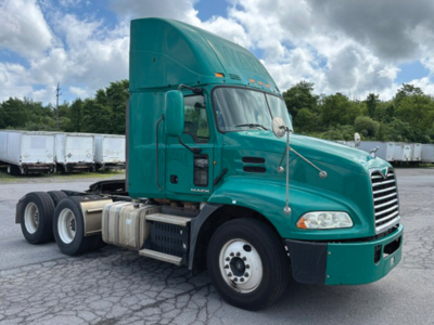 Truck cab with green Mack CXU613 6x4 tractor in a parking lot, side view showing fuel tanks, steps, and front grille.