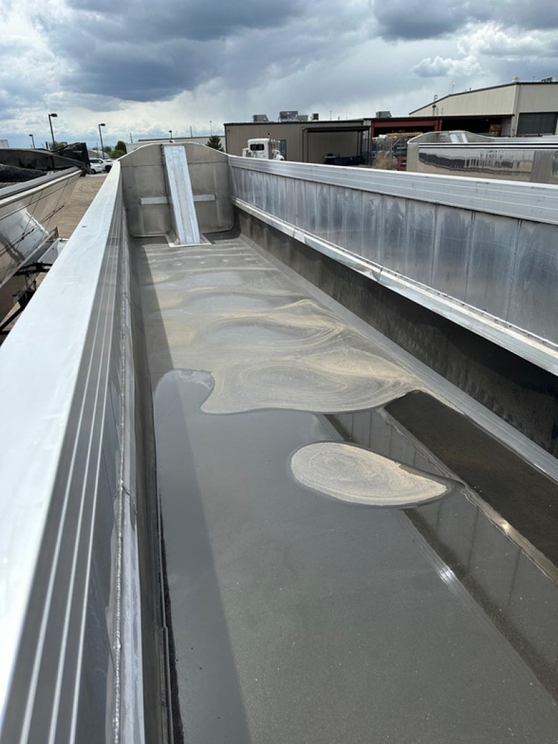 Trailer bed of a 2026 Mac Western light weight aluminum end dump showing a glossy aluminum surface with sand-like residue.